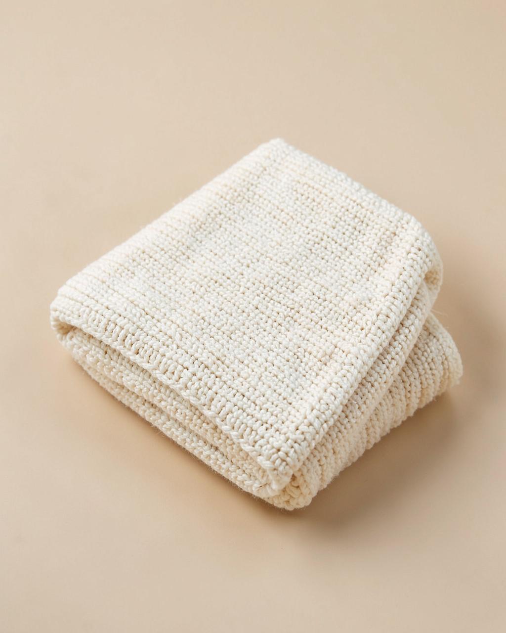 Plaid en maille crème plié sur fond beige clair