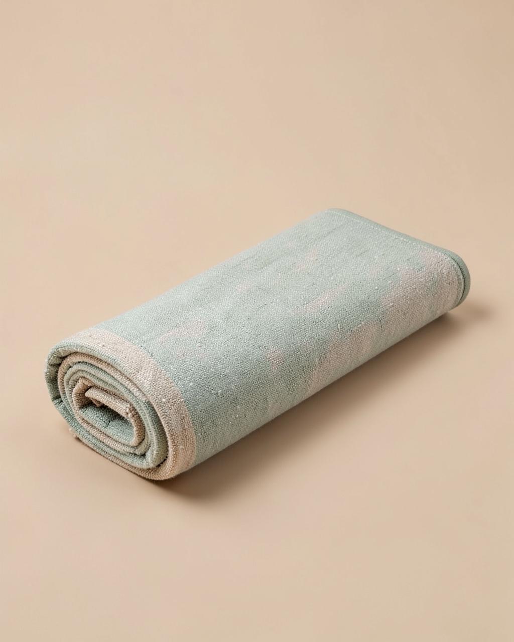 Tapis lifestyle en coton tissé vert sauge roulé sur fond beige clair